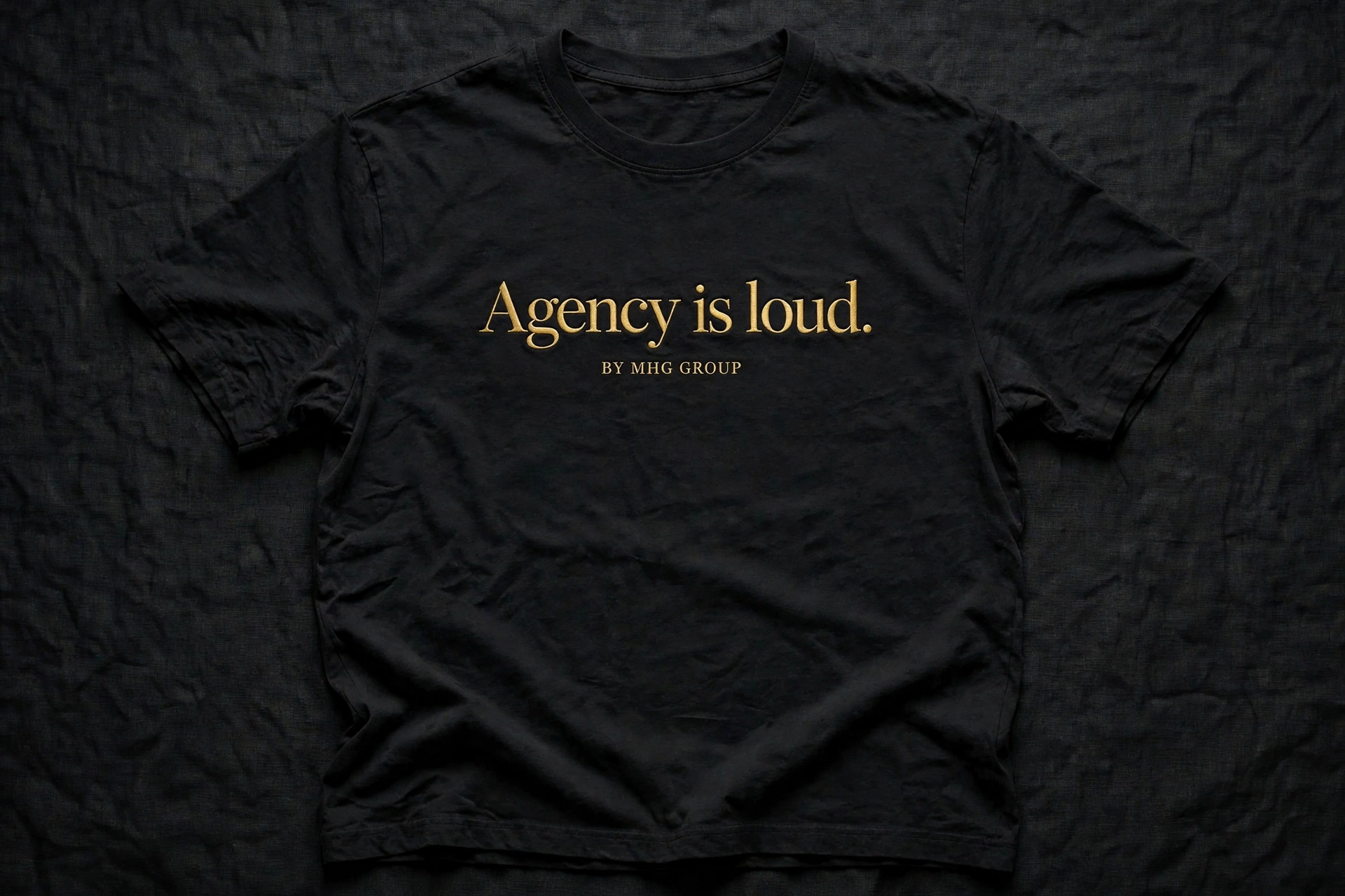Black T-shirt with Agency is loud in gold serif lettering and By MHG Group beneath