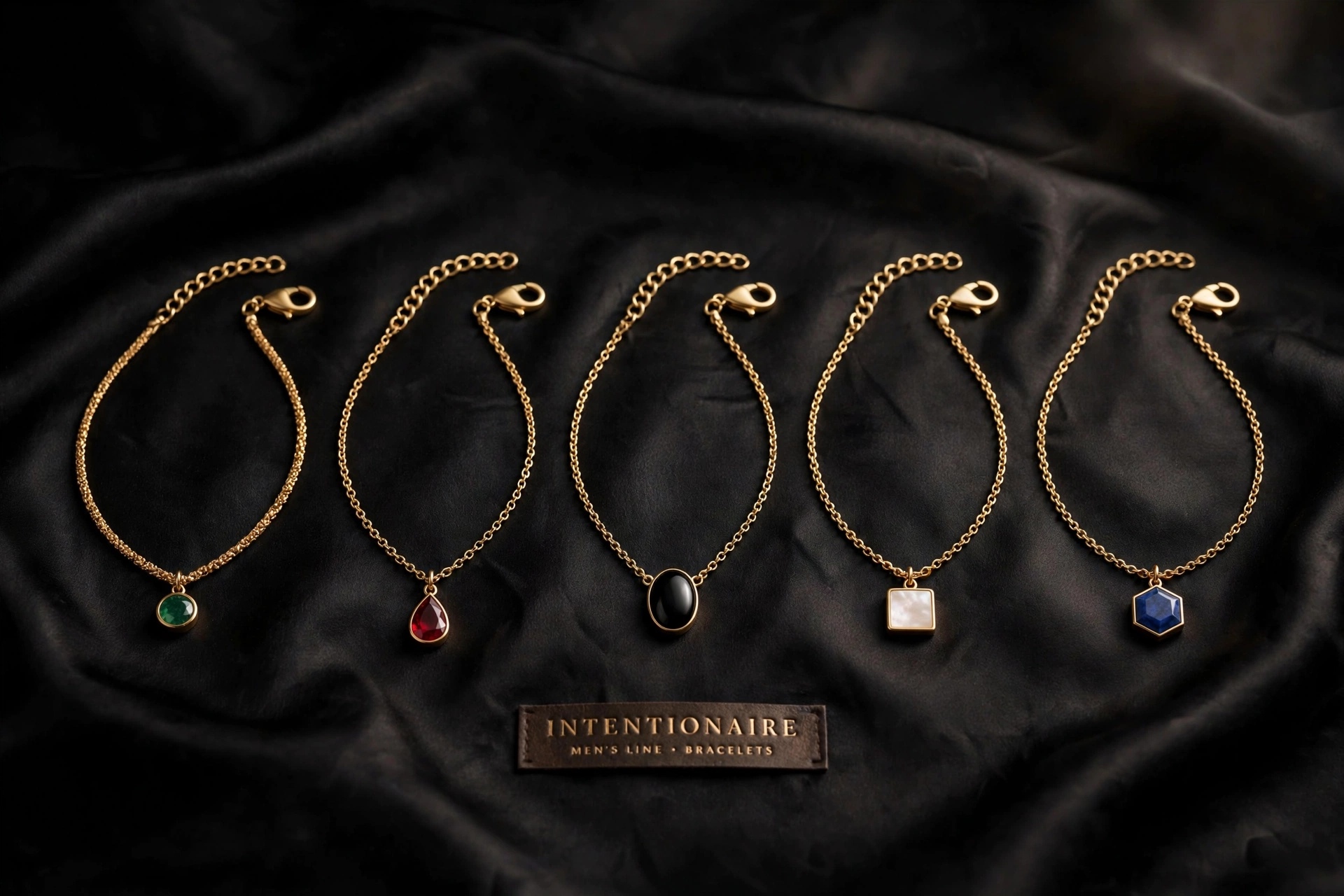 Five men's chain bracelets on black satin with small round green, teardrop red, oval black, square ivory and hexagon blue charms